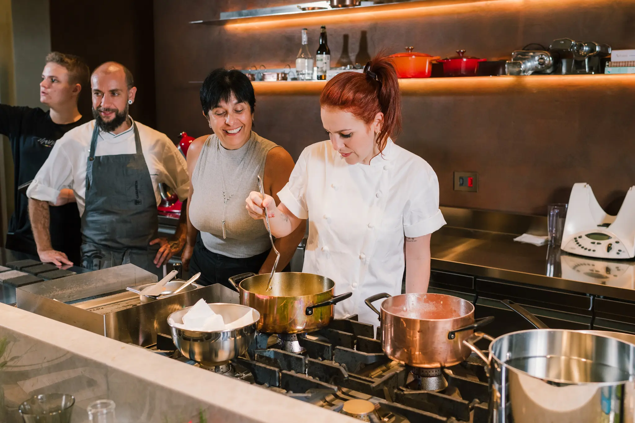 Registro de uma das edições do Encontros na Cozinha, aulas expositivas com a chef Sofia Marinho. Na imagem, Sofia demonstra o cozimento de um prato, enquanto alunos a observam.